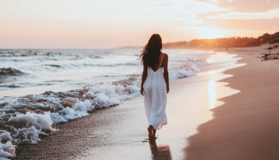 夕焼けの浜辺を歩く白いドレスの女性